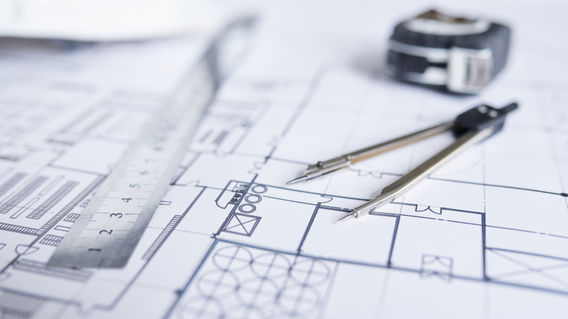 Architectural blueprints with ruler, compass, and tape measure used for Denali Customs project planning